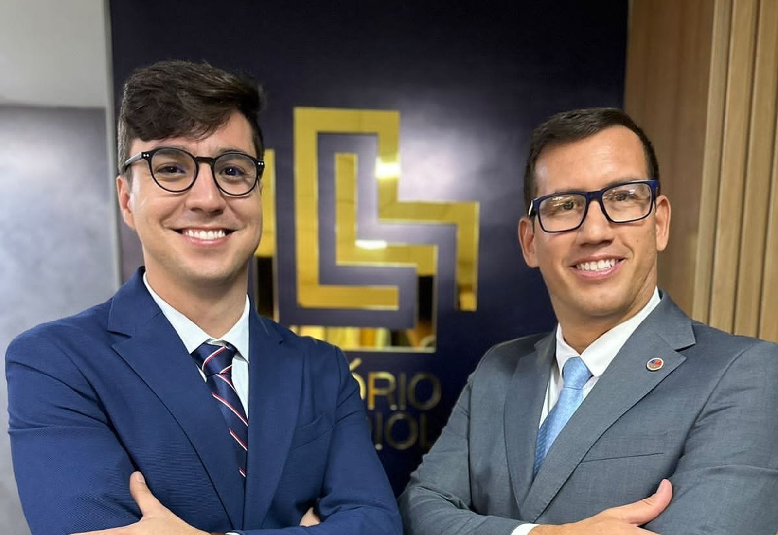 Diogo Loiola e Afonso de Ligório lado a lado, diante da parede com o monograma do escritório em relevo dourado
